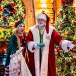 Santa and an elf in front of the Christmas tree with gifts