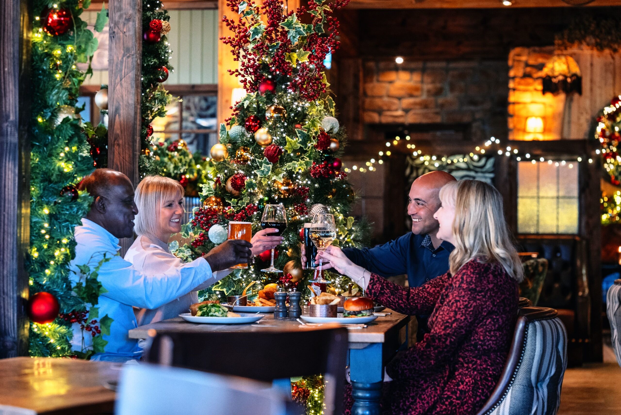 Four people clinking glasses with Christmas decorations in the background